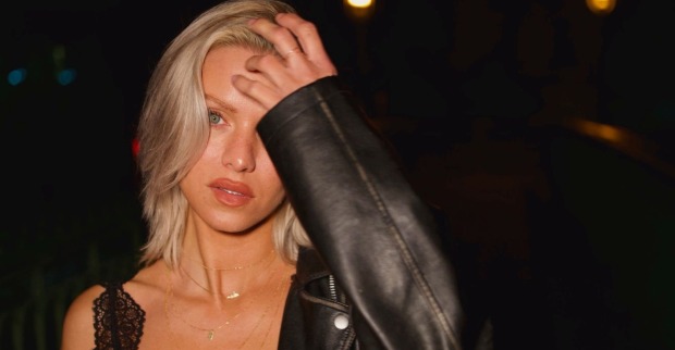 blonde junge Frau in einer schwarzen Lederjacke hält sich die linke Hand an die Stirn
