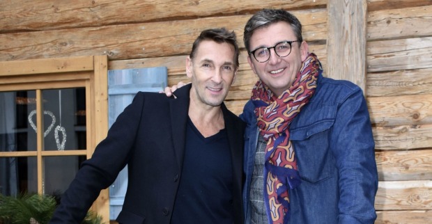„Bergdoktor“-Stars Mark Keller und Hans Sigl stehen gemeinsam vor einer Holzhütte.