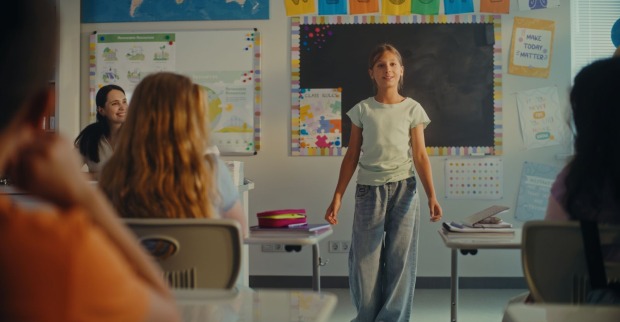 Ein Mädchen steht vor einer Klasse und sagt etwas zu ihnen.
