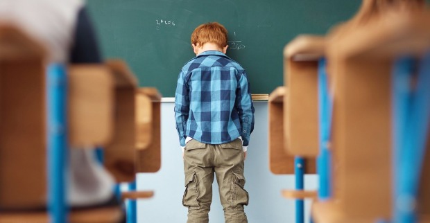 Ein Bub lehnt mit dem Kopf an einer Tafel.