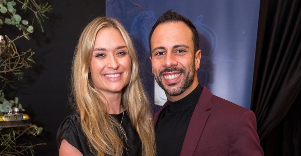 Corinna Kamper und Danilo Campisi posieren gemeinsam bei einer Veranstaltung. Die ehemalige Rennfahrerin trägt Schwarz, ihr Ehemann einen bordeauxroten Anzug.
