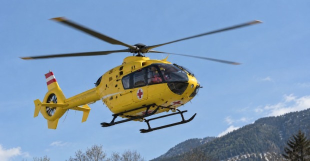 Gelber Rettungshubschrauber im Flug vor einer Bergkulisse als Symbolbild zum schweren Gerüst-Unfall in Debant in Osttirol.