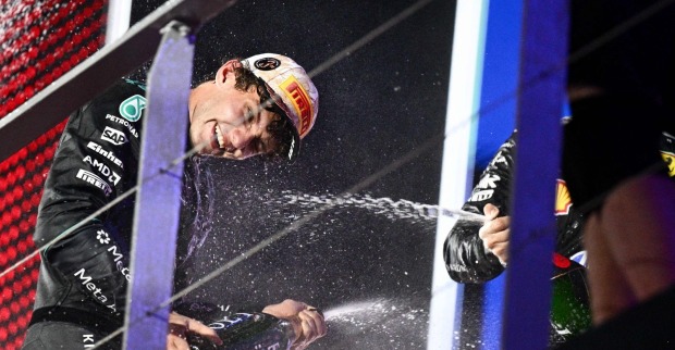 Kimi Antonelli im schwarzen Mercedes-Rennanzug und mit Pirelli-Kappe spritzt bei einer Formel-1-Siegerehrung lachend Champagner.