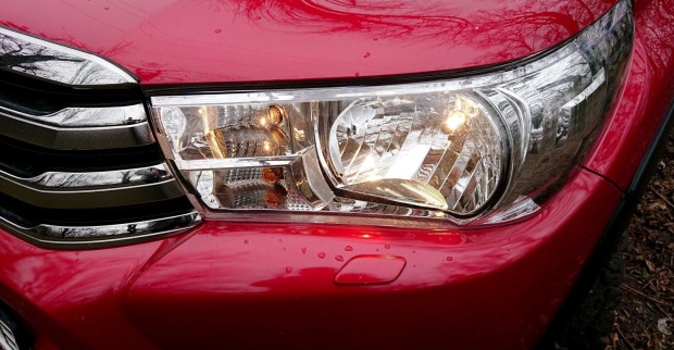 Nahaufnahme eines eingeschalteten Autoscheinwerfers an einem roten Pkw bei Tageslicht
