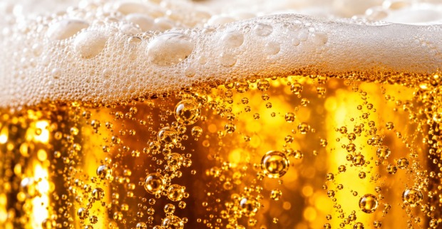 Makroaufnahme von goldgelbem Bier mit weißer Schaumkrone und aufsteigenden Kohlensäurebläschen.