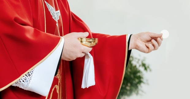 Hände eines katholischen Priesters mit einer Oblate und Wein