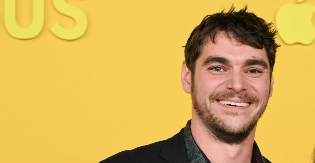 RJ Mitte, bekannt als Walter White Jr. aus „Breaking Bad“, lächelt bei einer Veranstaltung vor gelbem Hintergrund in die Kamera.