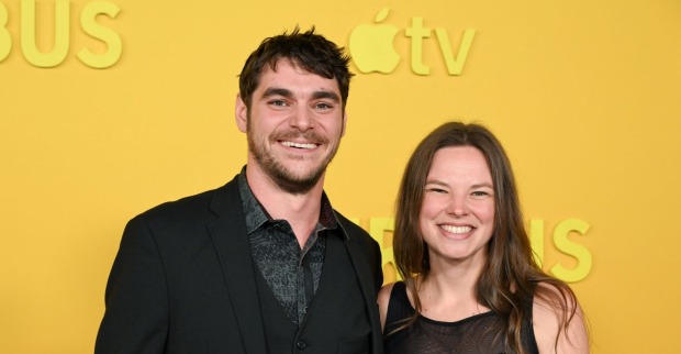 RJ Mitte und seine Verlobte Kennedy Suarez lächeln gemeinsam bei einer Veranstaltung vor einer gelben Apple-TV-Kulisse in die Kamera.