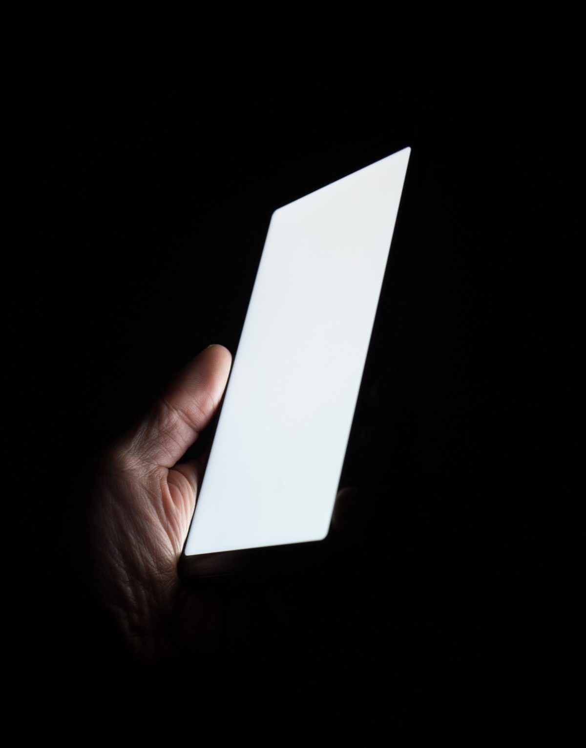 Eine Hand hält ein Smartphone mit hellem Display vor einem schwarzen Hintergrund.