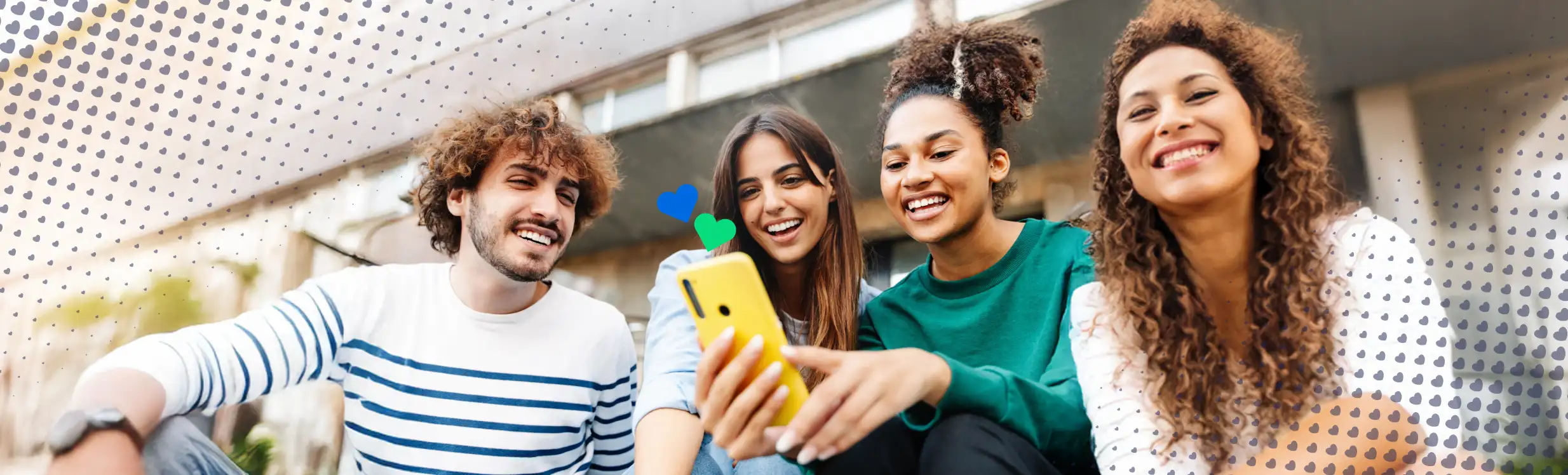 Four international students smiling and sharing a smartphone together outdoors