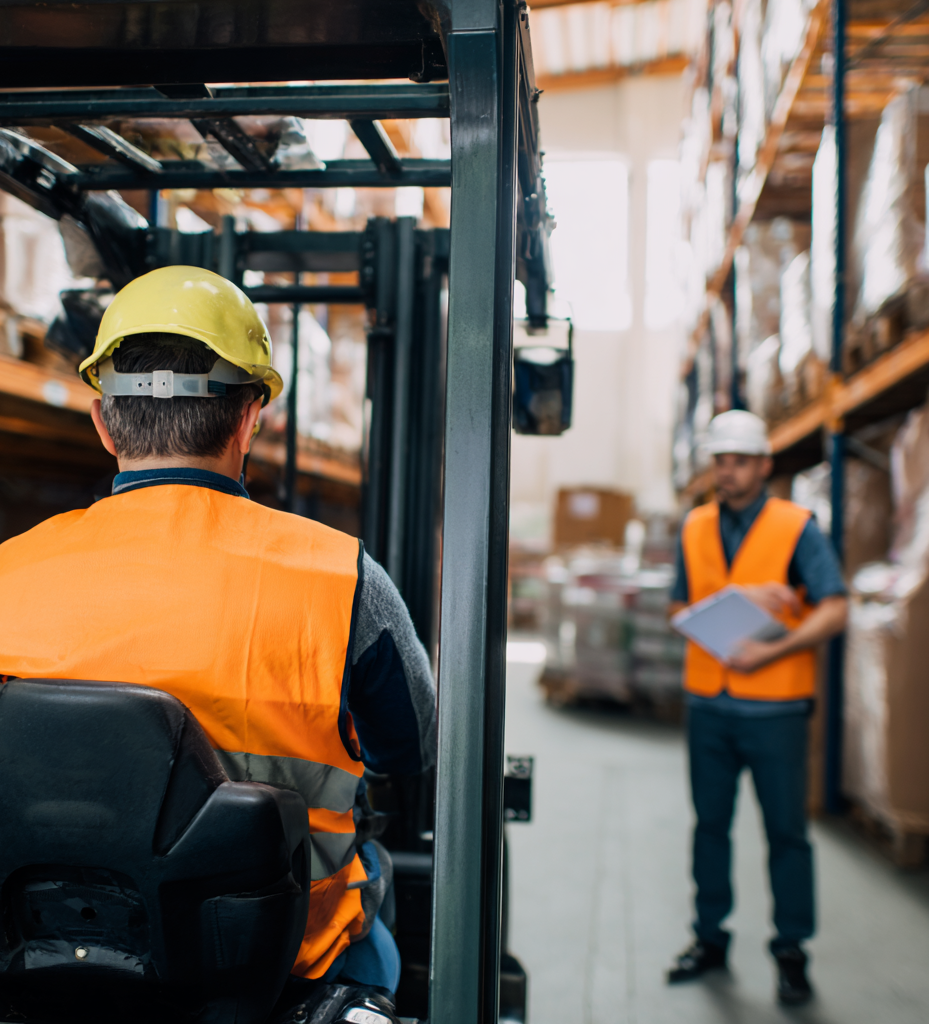 Instructeur legt aan cursist uit hoe lang een heftruckcertificaat geldig is tijdens een praktijktraining met heftruck in magazijn.