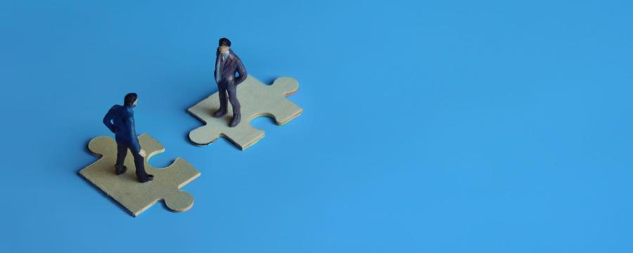 Blauer Hintergrund, Puzzleteile, zwei Männer: Symbol für Firmenübernahme