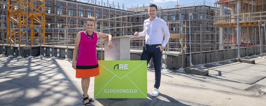 Village im Dritten: ARE Geschäftsführerin Christine Dornaus hat das Gleichengeld an Prokurist Danijel Krajina, den stellvertretenden Niederlassungsleiter von Swietelsky, übergeben. Die beiden stehen auf der Terrasse des ANCHOR mit Blick auf die dahinterliegenden Wohnungen.