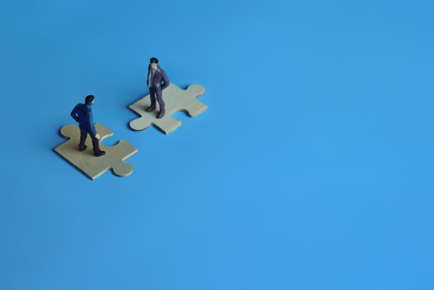 Blauer Hintergrund, Puzzleteile, zwei Männer: Symbol für Firmenübernahme