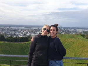 Zwei Frauen stehen auf dem Mount Eden mit der Skyline Aucklands im Hintergrund.