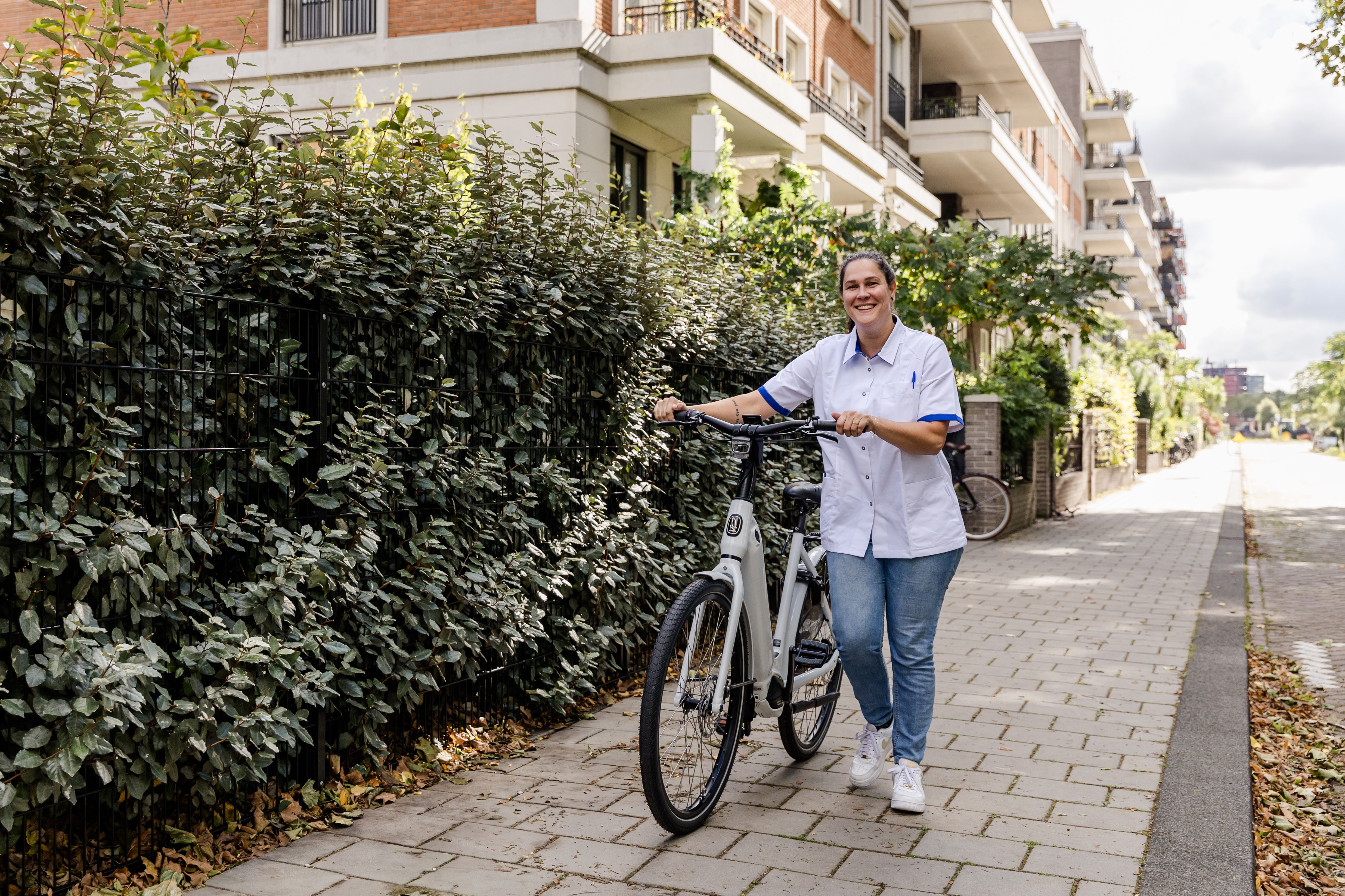 Lachende zorgmedewerker met fiets aan de hand.