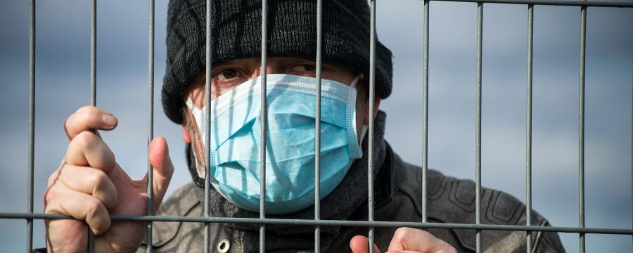 Ein Mann mit Maske hinter einem Zaun.