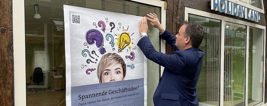 Bürgermeister von Hameln bringt Werbeplakat für Aktion Hameln Handelt an