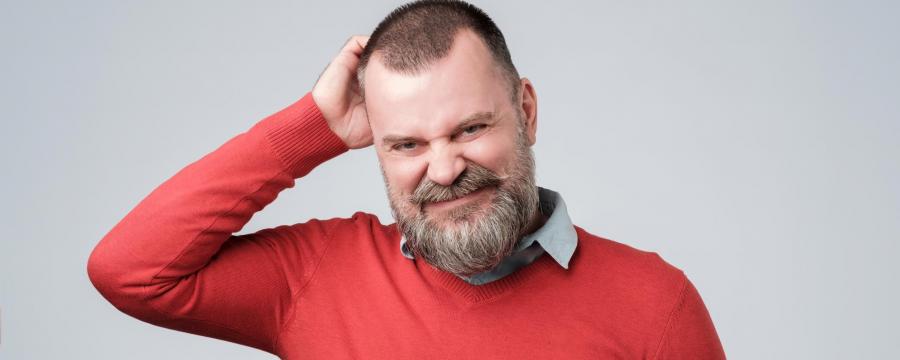 Mann mit rotem Pullover kratzt sich verwirrt am Kopf.