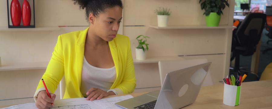 Frau sitzt mit Bauplan vor Notebook