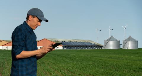 Farmer with tablet computer on a background of modern dairy farm using renewable energy, solar panels and wind turbines