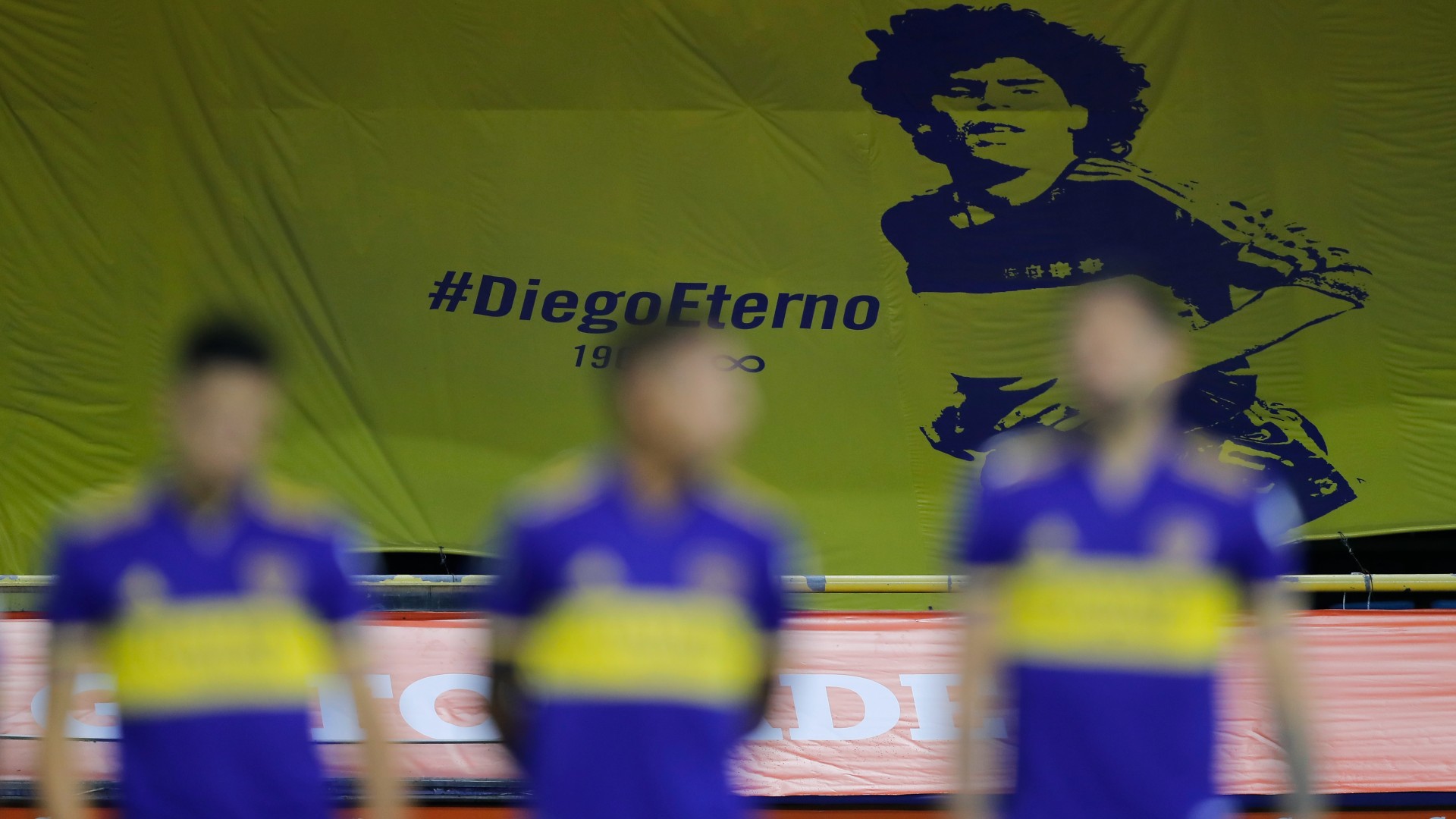Boca players in front of the banner dedicated to Diego Maradona (©Juan Ignacio Roncoroni - Pool/Getty Images)