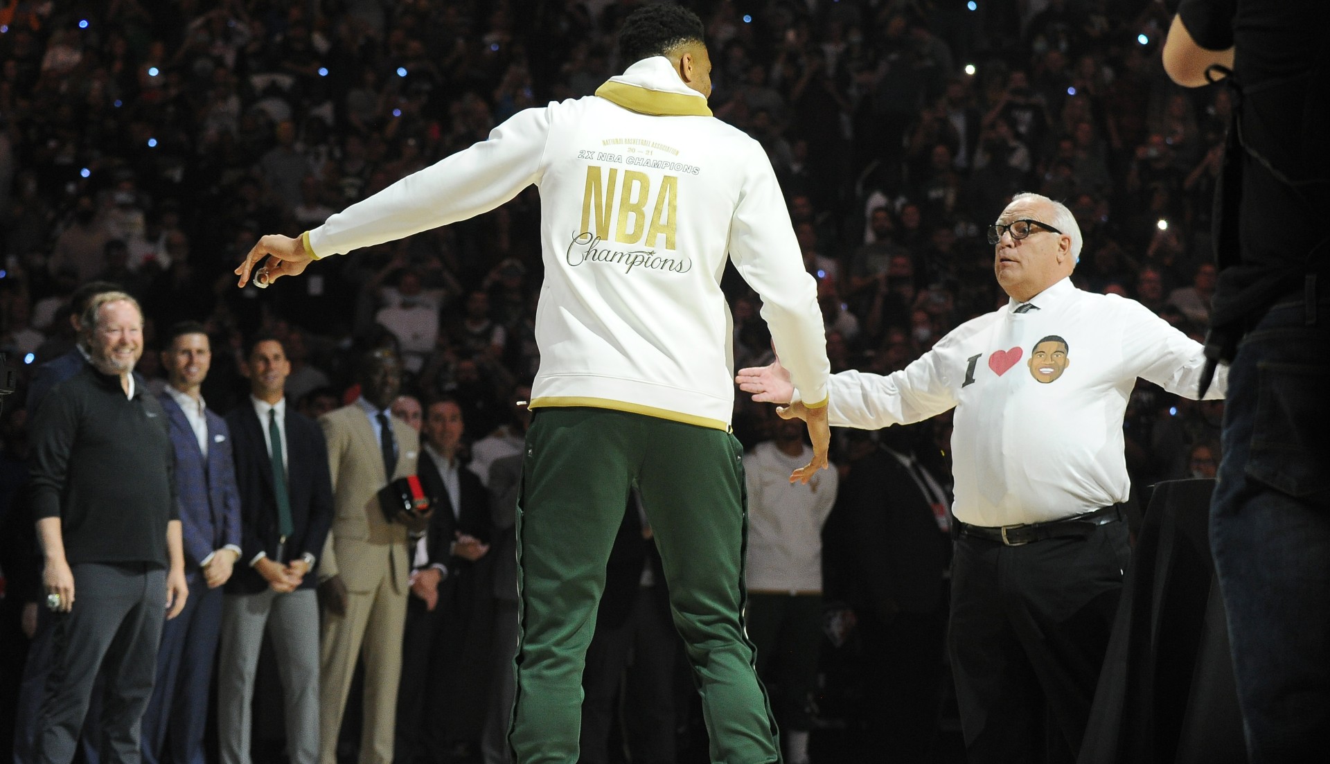 Former announcer Jim Paschke shows Milwaukee Bucks forward Giannis Antetokounmpo (34) his shirt after receiving his NBA championship ring at Fiserv Forum (©Michael McLoone-USA TODAY Sports)