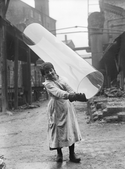 Female glass worker carrying a tube of rolled glass at Pilkington Glass Ltd., St Helen’s, 1918. The company still exists today