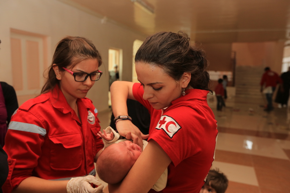 Syria: Humanity in Conflict at IWM North. SARC volunteers giving support to some of the 2,000 people displaced from Moaddamiyah, a besieged town in rural Damascus. In the shelter in Qudsaya, where the people were transferred, two SARC volunteers examine a