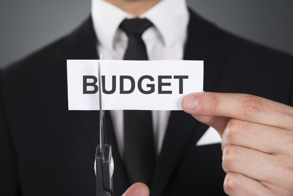 Businessman Cutting The Word Budget On Paper With Scissors