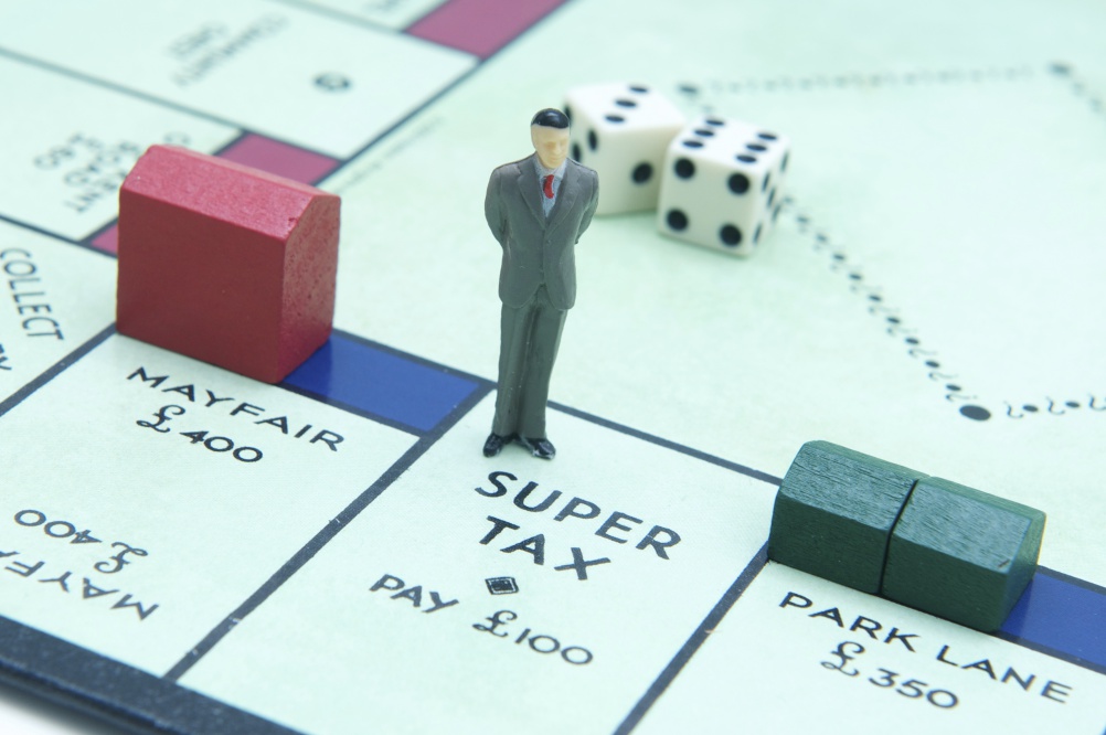 London, UK - July 2, 2011: Model figurine of a businesman standing at Super Tax on the board game monopoly Model figurine of a businesman standing at Super Tax on the board game monopoly with hotel on Mayfair and houses on Park Lane and Dice in the background