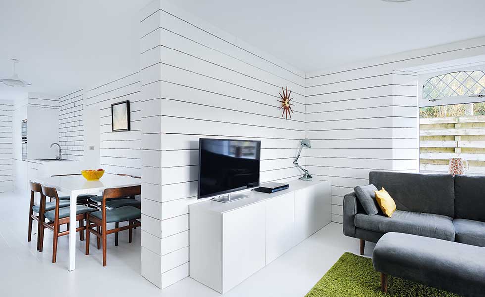 scandi style room with white panelled walls white tv stand and green rug