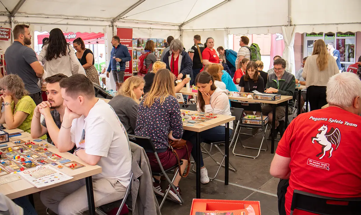 Menschen sitzen an Tischen in einem Zelt und spielen Brettspiele