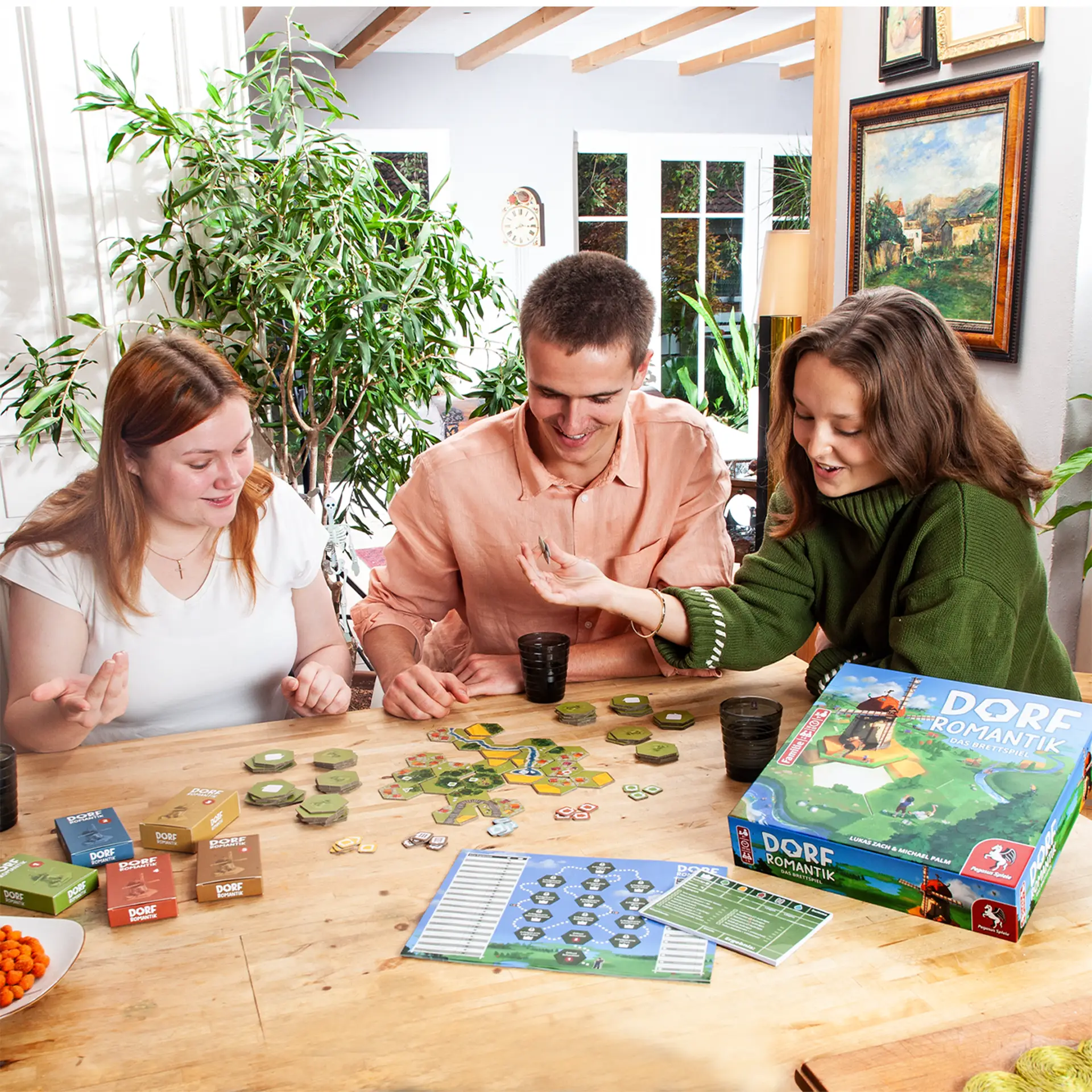 Drei Personen sitzen an einem Tisch und spielen Dorfromantik - Das Brettspiel