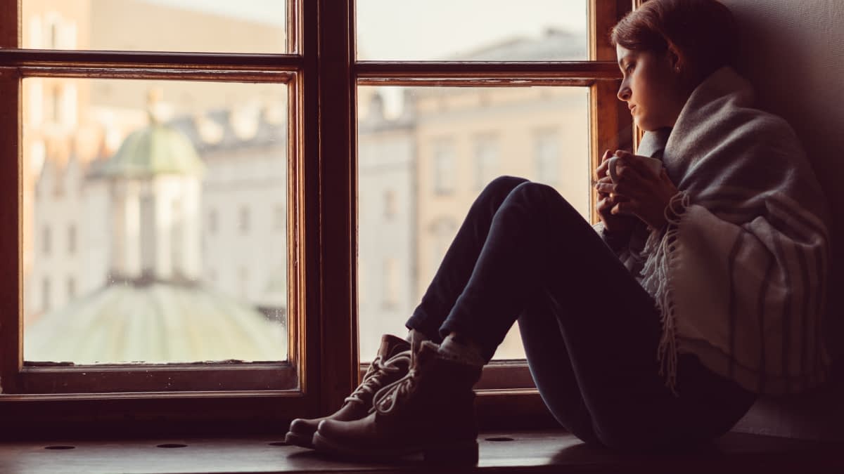 Junge Frau sitzt mit Teetasse auf Fensterbank 