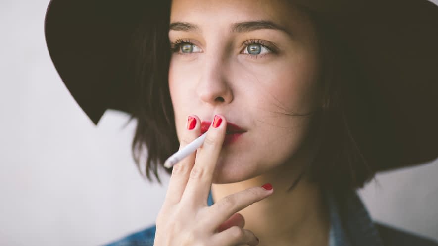 Eine junge Frau mit Hut zieht an einer Zigarette.