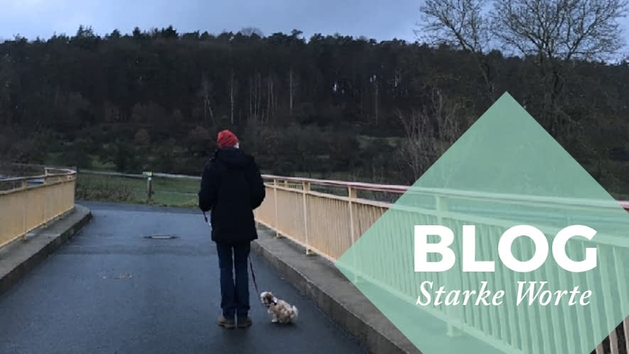 Starke Worte: Mann mit Hund auf einer Brücke an einem grauen Herbsttag