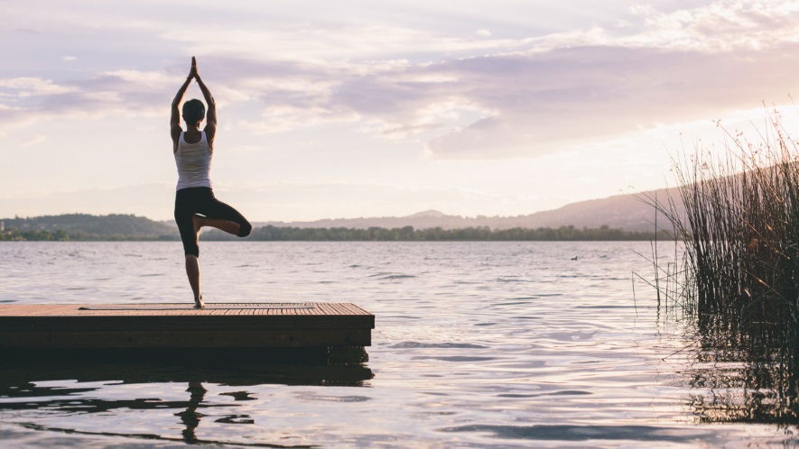 Yoga Übung der Baum auf einem Steg am Wasser