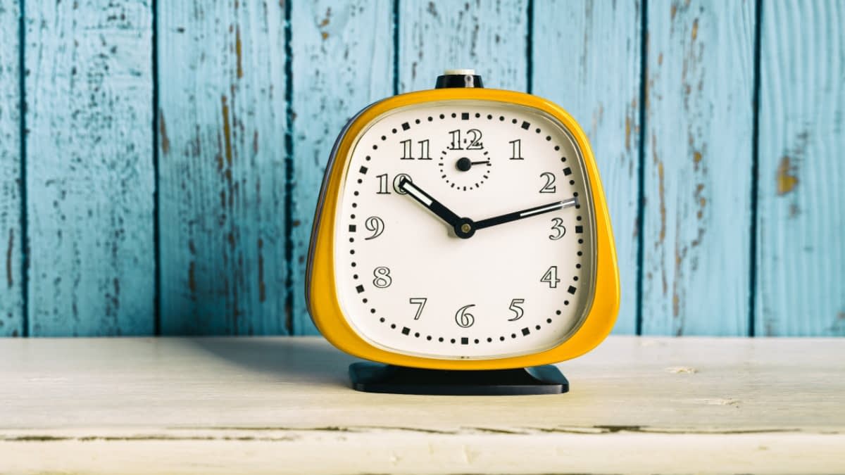 Gelber Wecker vor blauer Holzwand