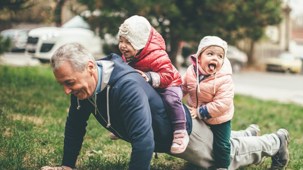 Älterer Herr macht Liegestütz mit Enkelkindern auf dem Rücken
