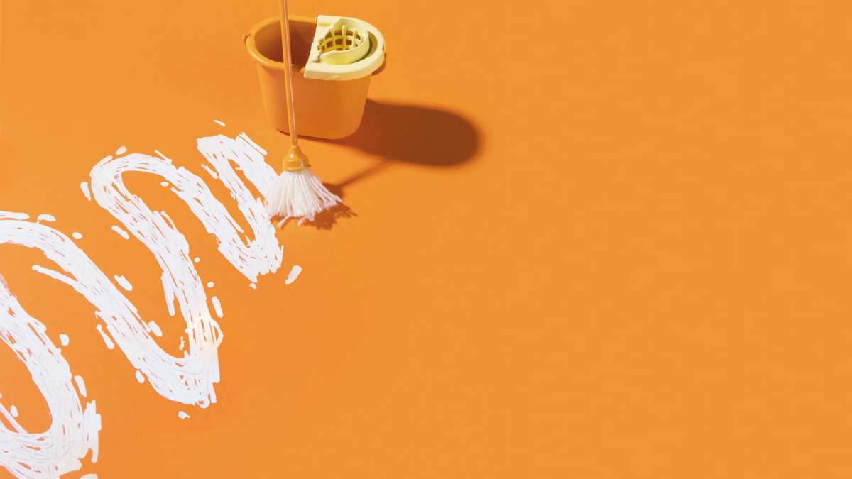 Eimer und Wischmob mit weißer geschlängelter Farblinie auf orangefarbenem Untergrund Eimer und Wischmob mit weißer geschlängelter Farblinie auf orangefarbenem Untergrund