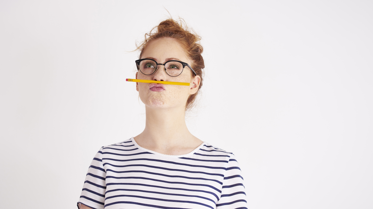 Frau mit Brille und gestreiftem Shirt balanciert Bleistift auf Oberlippe
