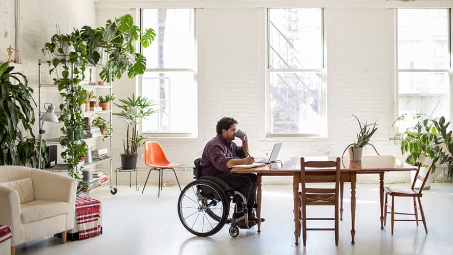 Mann im Rollstuhl sitzt am Tisch und trinkt Tee