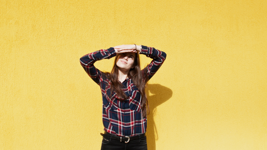 Frau schaut schräg nach oben und schützt ihre Augen vor der Sonne