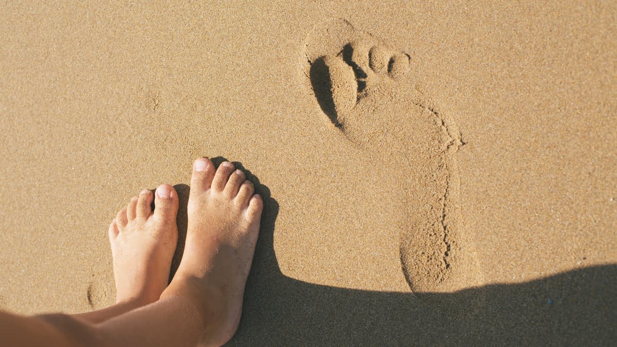 Füße im Sand neben Fußabdruck