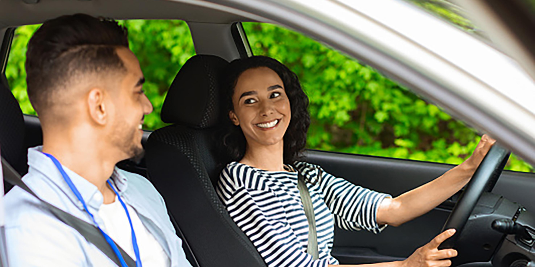 Excited young brunette woman sitting at driving car seat, looking at handsome arab man and smiling greeting instructor, female student of driving school ready for new lesson, side view