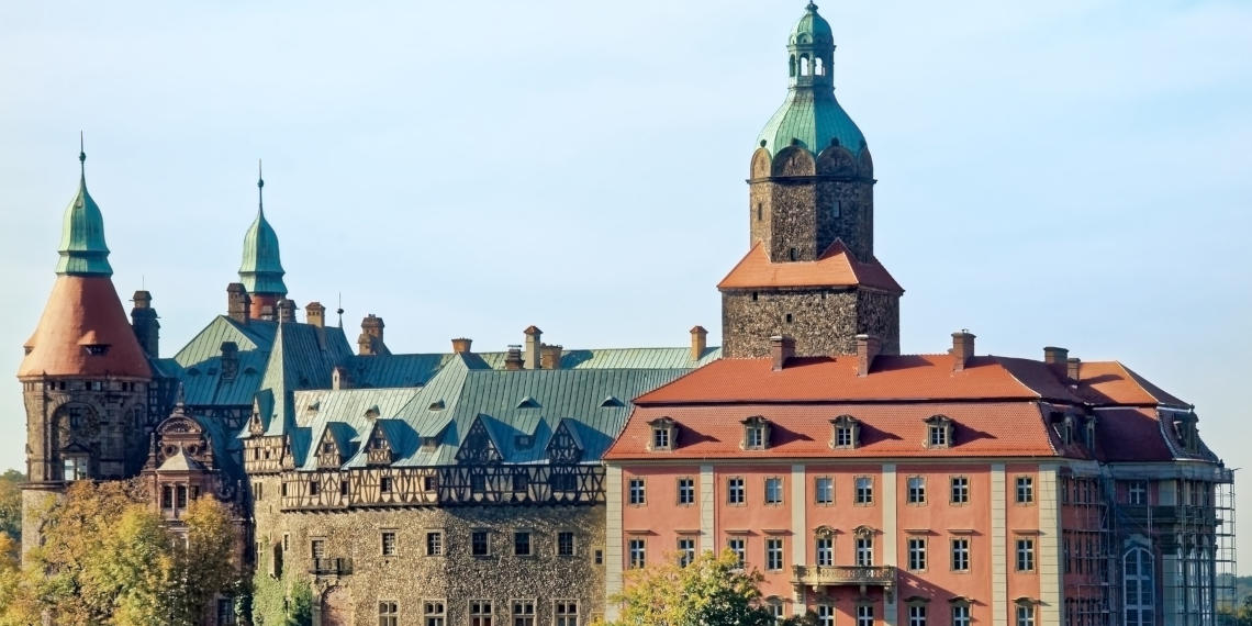 Podróżuj z FlixBusem do zamku w Wałbrzychu i podziwiaj krajobrazy Stary kamienny zamek z różnymi wieżami i nowszą częścią w kolorze pomarańczowym