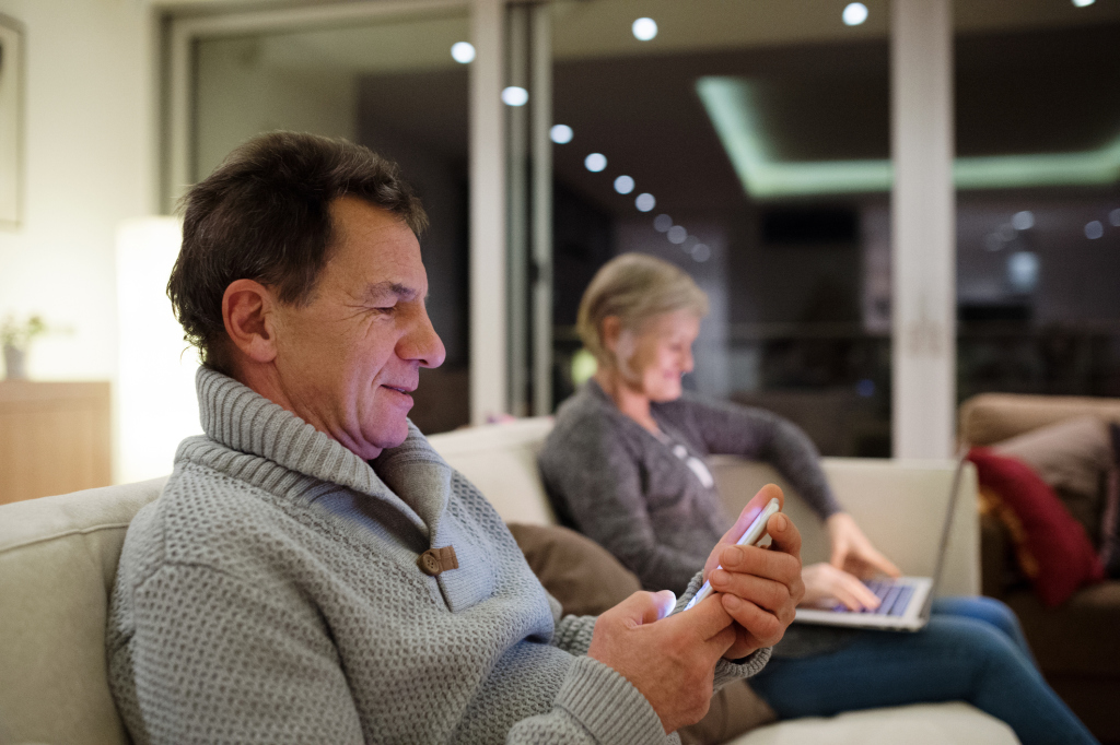 Älteres Ehepaar an Smartphone und Laptop auf dem Sofa Älteres Ehepaar an Smartphone und Laptop auf dem Sofa