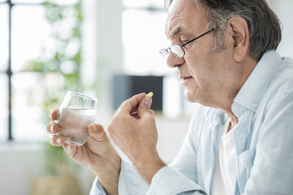 Älterer Mann nimmt Medikament mit einem Glas Wasser ein Älterer Mann nimmt Medikament mit einem Glas Wasser ein