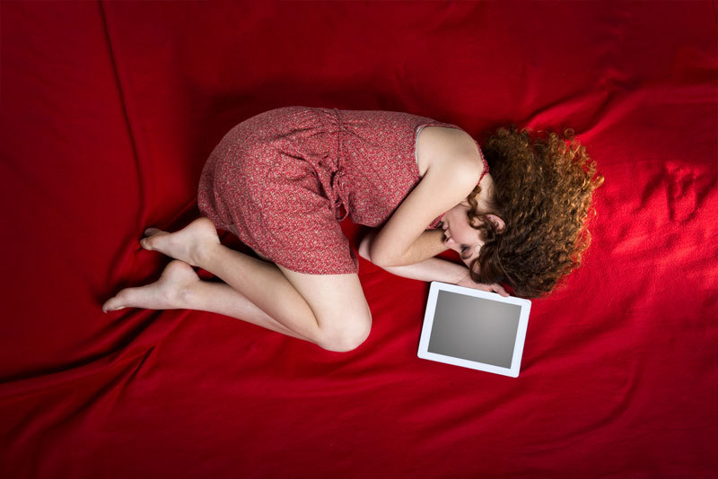 Frau liegt traurig auf einem Bett, neben ihr ein Tablet Frau liegt traurig auf einem Bett, neben ihr ein Tablet